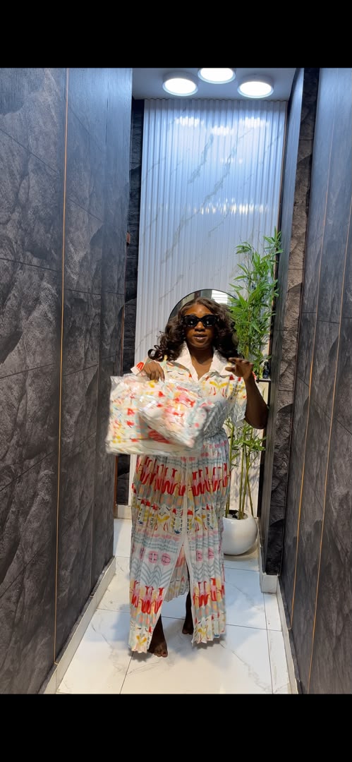 Woman wearing white graphic print co-ord shirt and wide-leg trouser set with matching tote bag